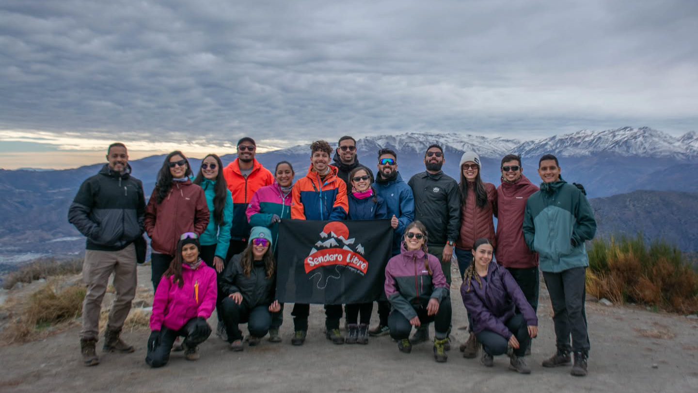 Integrantes de Sendero Libre posando con el lienzo del club en una cumbre, con la cordillera nevada al fondo