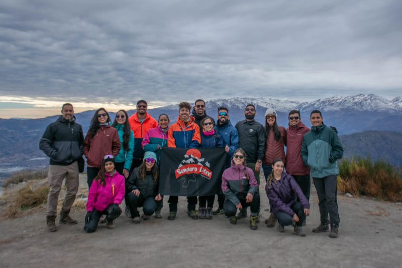 Integrantes de Sendero Libre posando con el lienzo del club en una cumbre, con la cordillera nevada al fondo