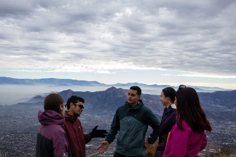 Un guía conversa con cuatro participantes en una cumbre, con Santiago a sus pies